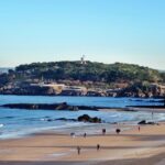 Familia disfrutando de un día soleado en la Playa de San José, con sombrillas y niños jugando en la orilla.